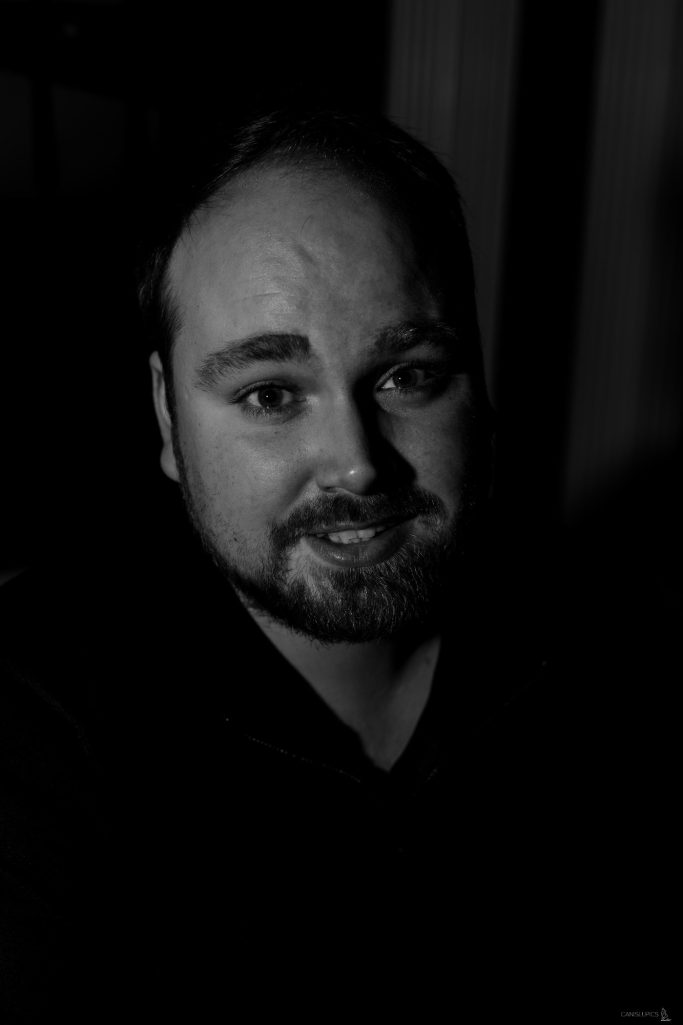 Portrait eines lächelnden Mannes mit Bart in dunkler Umgebung.